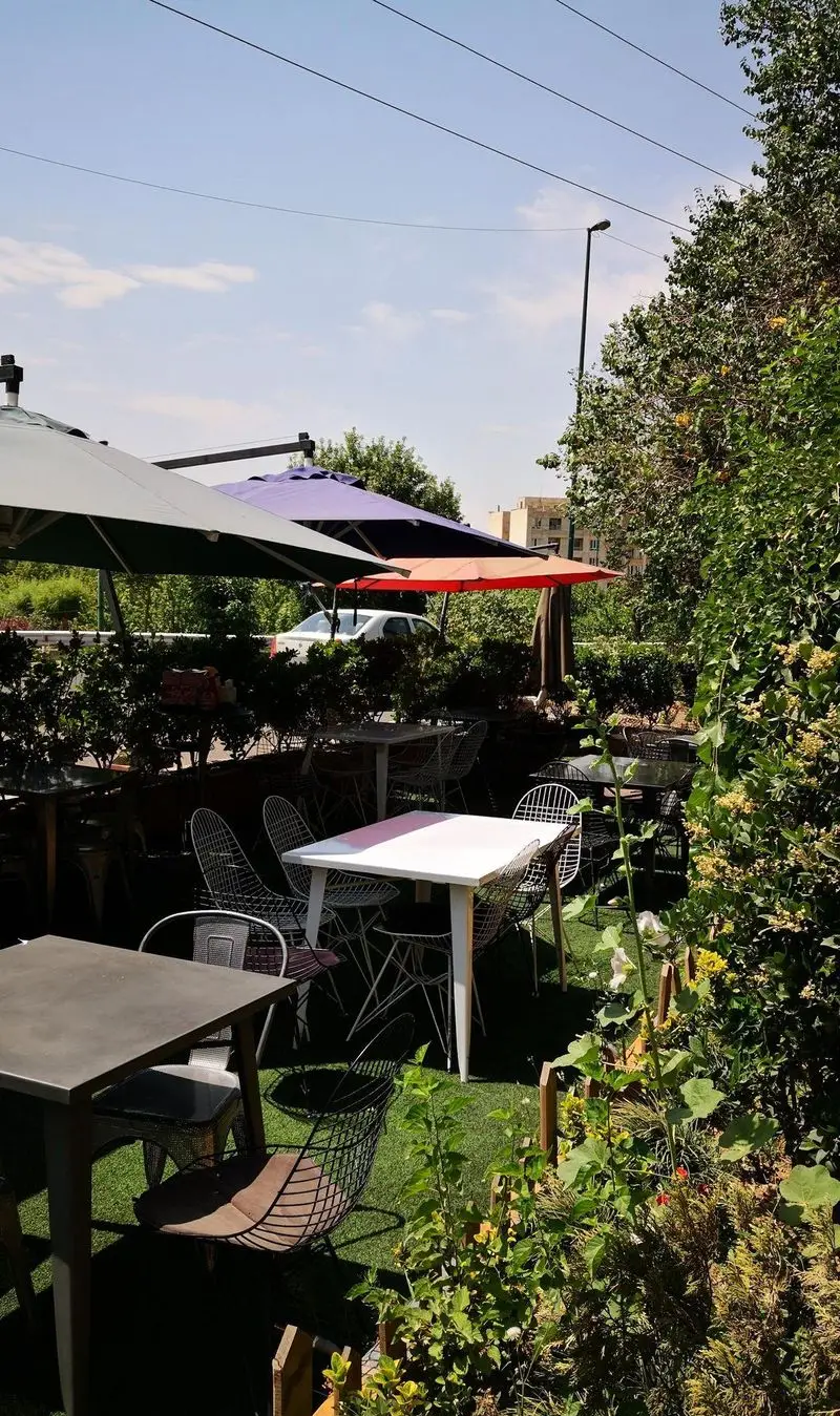 فضای باز رستوران سرزمین سوخاری با میز و صندلی‌های مدرن، چترهای رنگی، فضای سبز دلنشین و آفتابی مناسب اوقات فراغت.