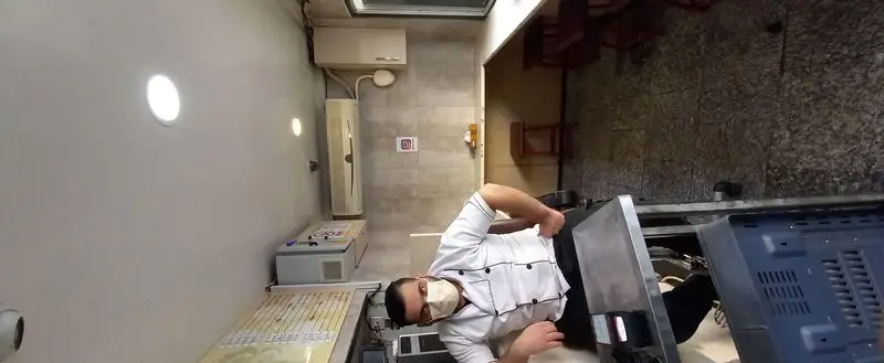 آشپز حرفه‌ای فست‌فود ترنج با رعایت کامل بهداشت (ماسک)، در آشپزخانه‌ای مدرن مشغول آماده‌سازی سفارشات. کیفیت و سرعت در ترنج.