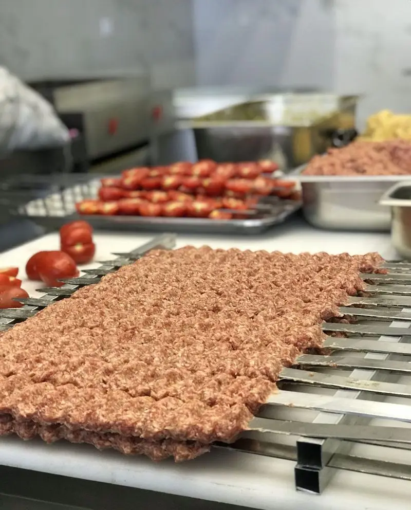 آماده‌سازی کباب کوبیده با گوشت چرخ‌کرده تازه روی سیخ در آشپزخانه رستوران تأیید، در کنار گوجه‌فرنگی‌های سیخ شده.