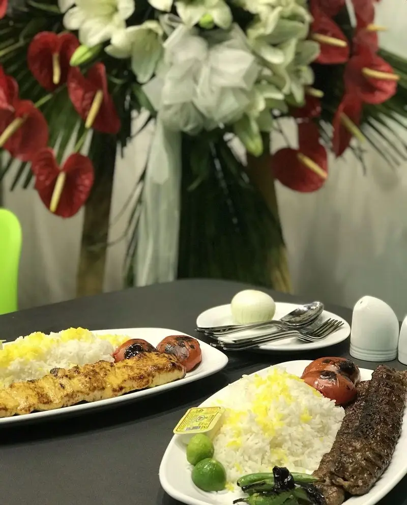 تصویری از میز غذای رستوران تأیید شامل کباب کوبیده و جوجه کباب، برنج زعفرانی، گوجه کبابی و لیمو تازه در محیطی زیبا.