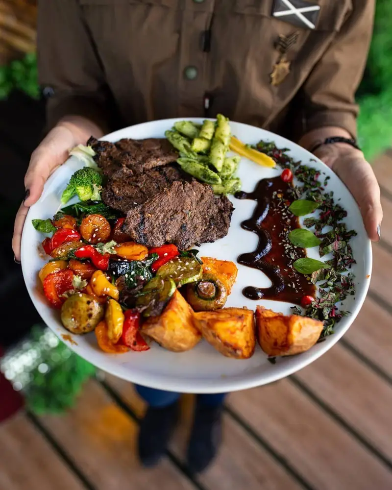 سرو استیک لذیذ در کافه ماها: بشقاب گوشت گریل شده، پاستا پستو، سبزیجات تازه و سیب زمینی شیرین. انتخابی سالم و خوش‌طعم.