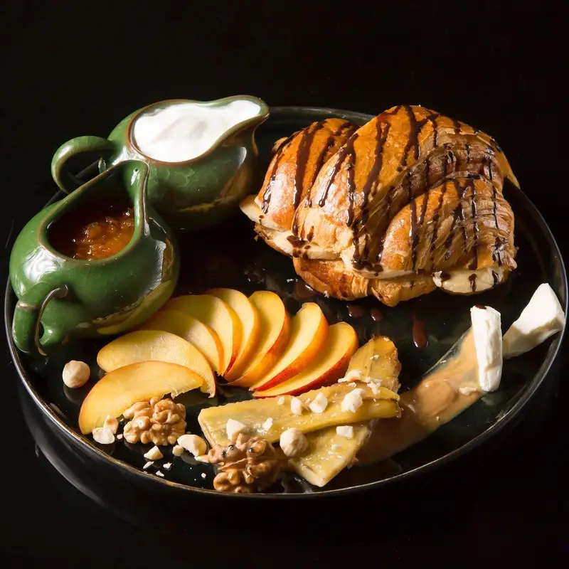 بشقاب صبحانه کافه ماها: کروسان پر شده با موز و سس شکلات، میوه‌های تازه، موز کاراملی، پنیر، مربا، خامه و مغزها. برانچی لذیذ.