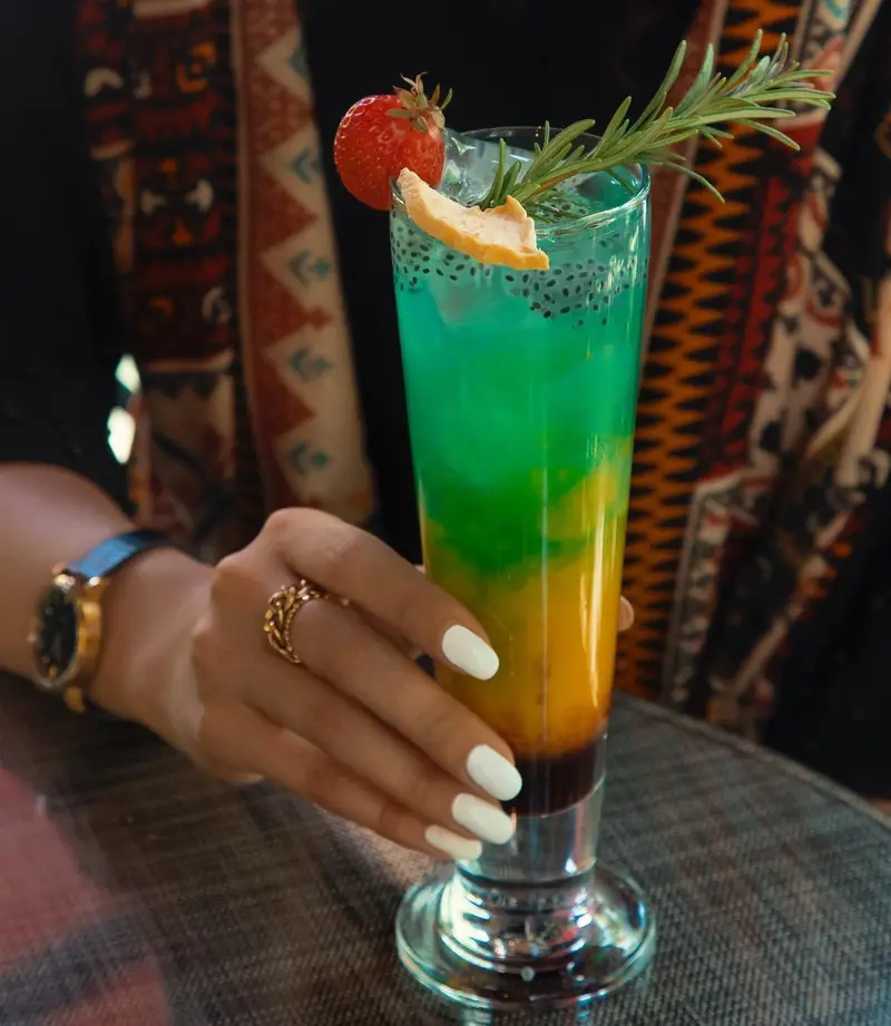 کوکتل رنگی و خنک کافه ماها با لایه‌های متنوع، تزیین شده با توت فرنگی، رزماری و تخم شربتی، انتخابی خاص و گوارا.