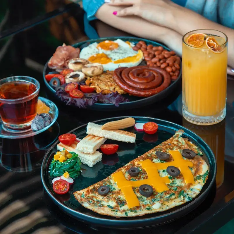 صبحانه مجلل و متنوع کافه ماها شامل املت، سوسیس، تخم مرغ، لوبیا، نان تست، سبزیجات تازه، چای و آب پرتقال. ایده‌آل برای برانچ.