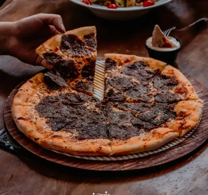 لذت چشیدن پیتزا شکلاتی خاص و خوشمزه از امیر شکلات دارآباد، با رویه‌ای تیره و اشتهاآور، یک برش آماده سرو.