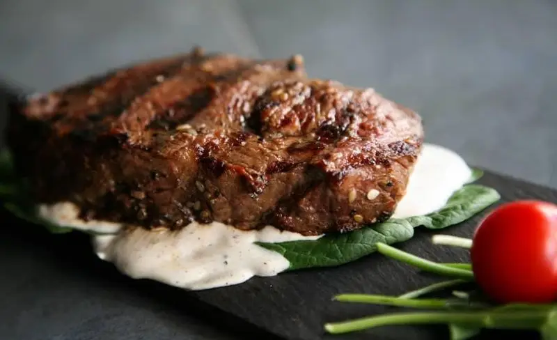 استیک گریل شده آبدار و خوشمزه با سس خامه‌ای و اسفناج تازه، انتخابی عالی از منوی اصلی کافه رستوران رپتور.