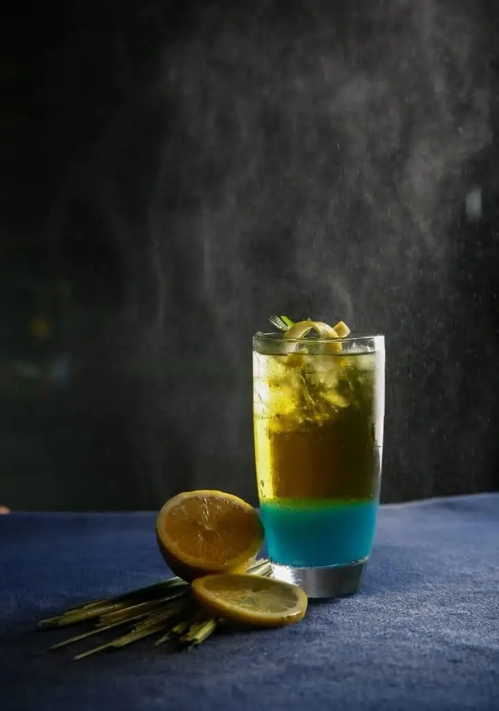 نوشیدنی خنک و شاداب با لایه‌های آبی و زرد، همراه با لیمو و نعنا در کافه رستوران رپتور، ایده‌آل برای یک تجربه گوارا و تابستانی.