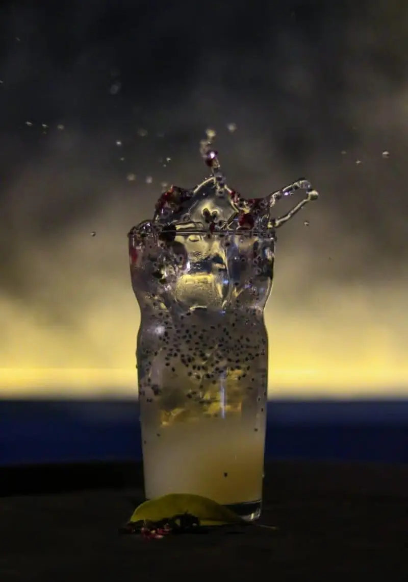 تصویری جذاب از نوشیدنی خنک و تازه کافه رستوران رپتور با اسپلش هیجان‌انگیز، شامل تخم شربتی، لیمو و تکه‌های میوه.