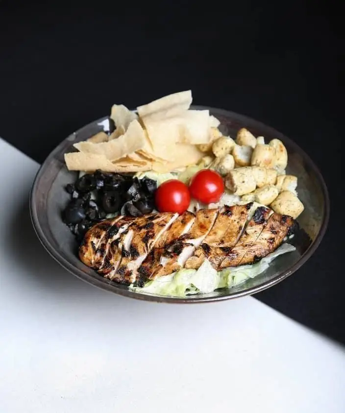سالاد مرغ گریل لذیذ با سینه مرغ برش‌خورده، زیتون، گوجه گیلاسی و نان ترد؛ ویژه کافه رستوران رپتور برای دوستداران غذای سالم.