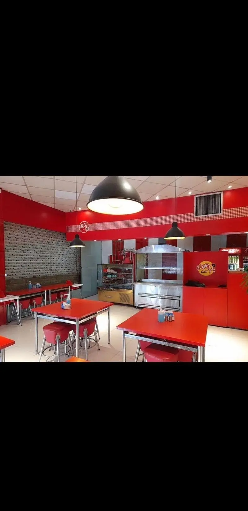 نمای داخلی فست فود بابا جون نارمک با دکوراسیون مدرن قرمز و سفید، شامل میز و صندلی‌های تمیز و آماده سرویس‌دهی به مشتریان است.