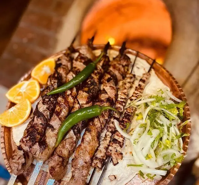 سفره‌ای پر از کباب‌های لذیذ و تازه جگرکی پاتوق شامل سیخ‌های گوشت و جگر، همراه با پیاز جعفری، فلفل و پرتقال، انتخابی عالی برای شام.