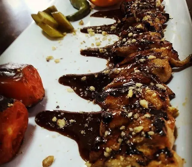 بلدرچین کبابی آغشته به سس مخصوص و گردو، در کنار گوجه کبابی و ترشی، غذایی استثنایی از کباب سرای آیدا.