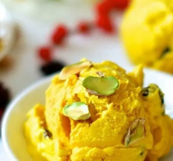 یک اسکوپ بستنی میوه‌ای خوشرنگ زعفرانی یا انبه با تزیین پسته در کاسه سفید، دسری تازه و خنک از آبمیوه و بستنی فروشی.