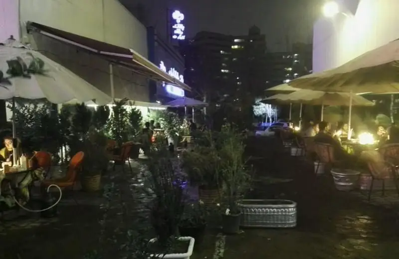 فضای باز دلنشین رستوران فرنگی ایوان در شب با مشتریانی که زیر چترها و کنار گیاهان شام می‌خورند، محیطی گرم و دعوت‌کننده.