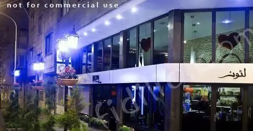 تصویر شب از نمای بیرونی کافه رستوران لئون با نورپردازی دلنشین، گلدان‌های گل و قلب‌های قرمز داخل پنجره‌ها، فضایی رمانتیک و جذاب.