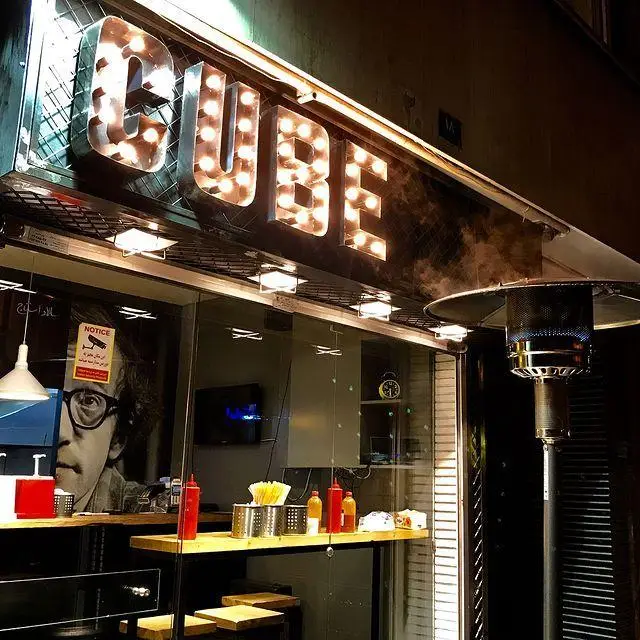 نمای شبانه رستوران کیوب برگر با تابلوی درخشان CUBE، گرماتاب بیرون و پیشخوان پر از چاشنی برای تجربه لذیذترین همبرگرها.