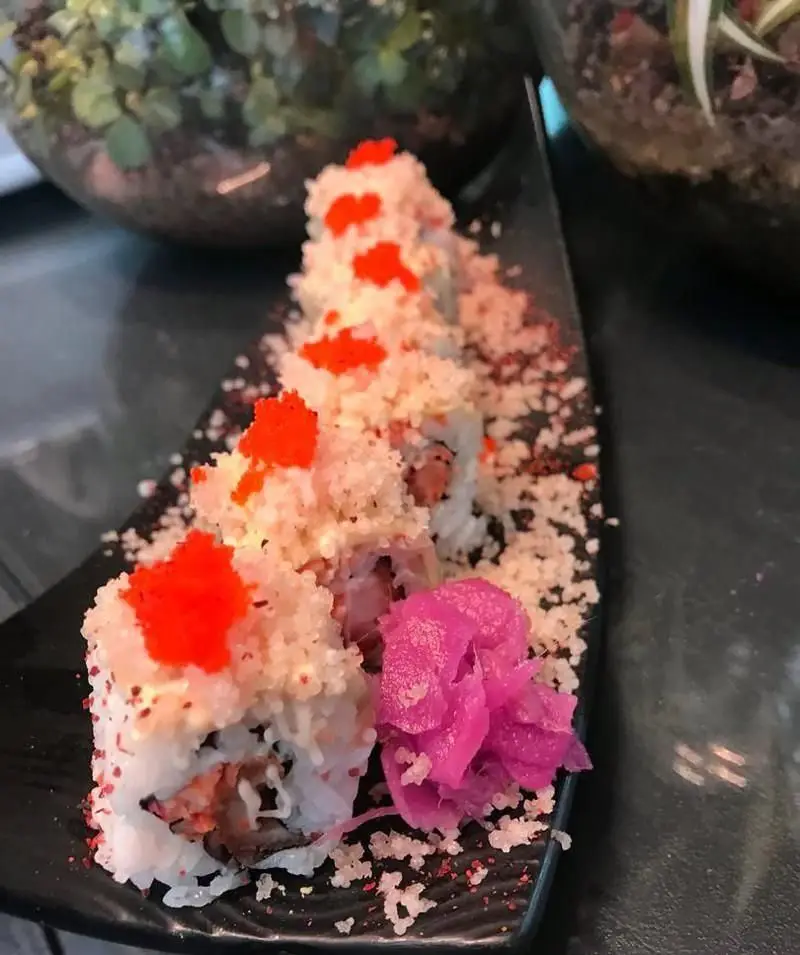 تصویر زیبا از رول‌های سوشی محبوب رستوران آسیایی الین سوشی با تاپینگ ترد و خاویار نارنجی، سرو شده با زنجبیل.