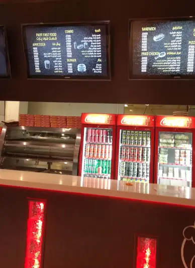 نمای داخلی فست فود پارت با منوی دیجیتال غذاهای متنوع شامل ساندویچ، برگر، پیتزا و نوشیدنی‌های خنک در یخچال‌های Coca-Cola.