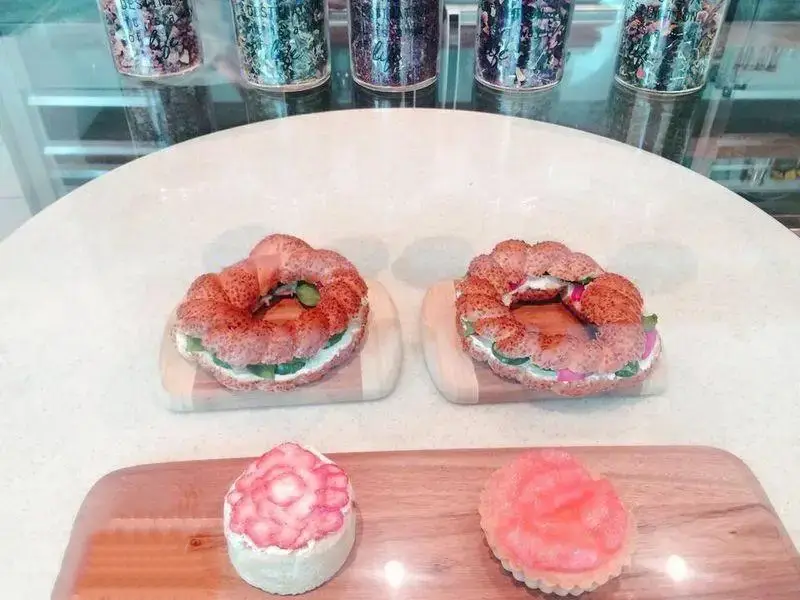 نمایی از میز کافه بارن با دو نان ساندویچی حلقوی خوشمزه، دسرهای شیرین توت فرنگی و تارت در فضای دلنشین کافه.