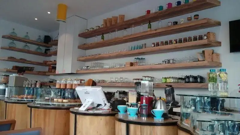 تصویری از داخل کافه بارن: قفسه‌های چوبی زیبا، ظروف متنوع، دستگاه‌های قهوه‌ساز، و ویترین‌های پر از شیرینی و کروسان تازه.