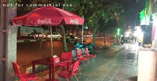 فضای باز رستوران چوپی برگر در شب: چتر کوکاکولا، میز و صندلی‌های قرمز، محیطی دلنشین کنار خیابان برای مشتریان.