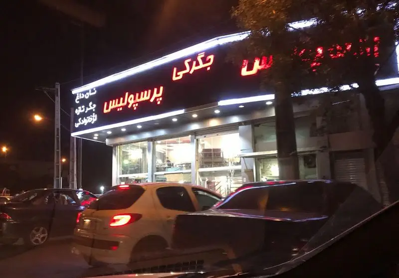 تصویر شبانه جگرکی پرسپولیس با تابلوهای نئون، نمایش نان داغ، جگر تازه، لخته و دل و قلوه، در فضای شهری.