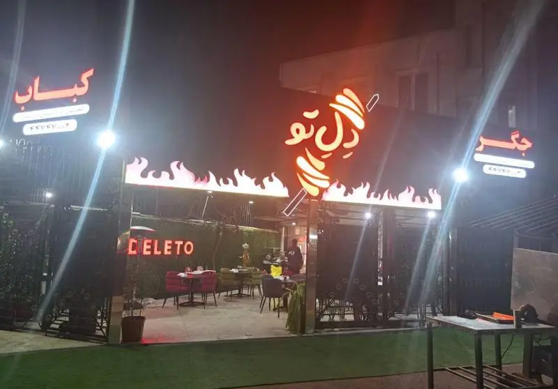 جگر سرای دل تو، رستوران کباب و جگر با تابلوهای نئونی شعله‌ور، فضای باز دلپذیر و طراحی مدرن در شب برای مشتریان.