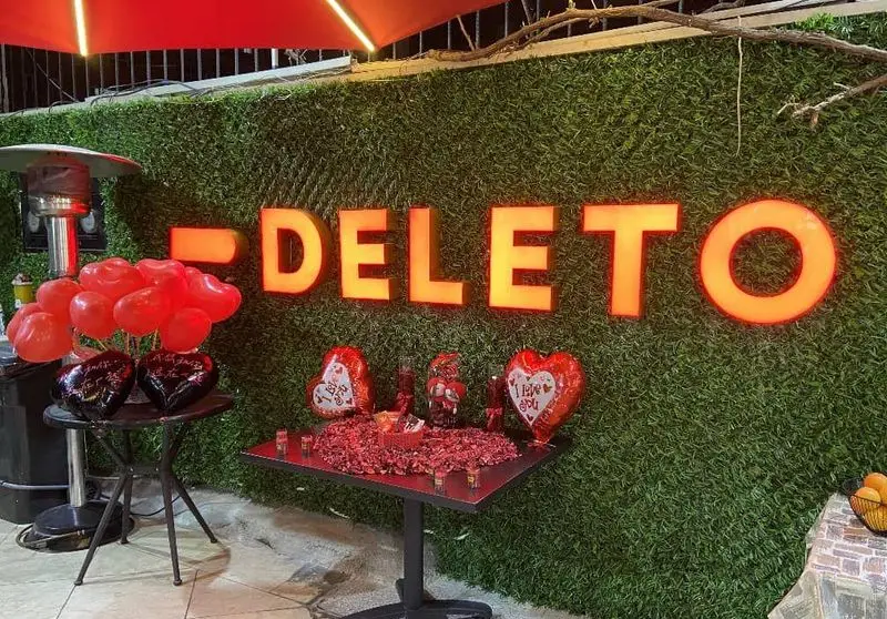 دکوراسیون رمانتیک جگر سرای دل تو با دیوار سبز، حروف درخشان DELETO، بالن‌های قلبی و گلبرگ‌های قرمز برای لحظات خاص.