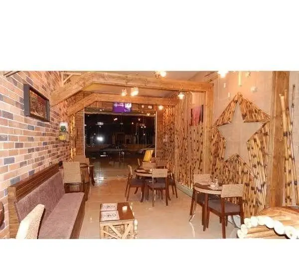 کافه ستاره: دکوراسیون داخلی جذاب با دیوار آجری، نیمکت و میز و صندلی‌های چوبی، تزئینات طبیعی بامبو با طرح ستاره بزرگ.