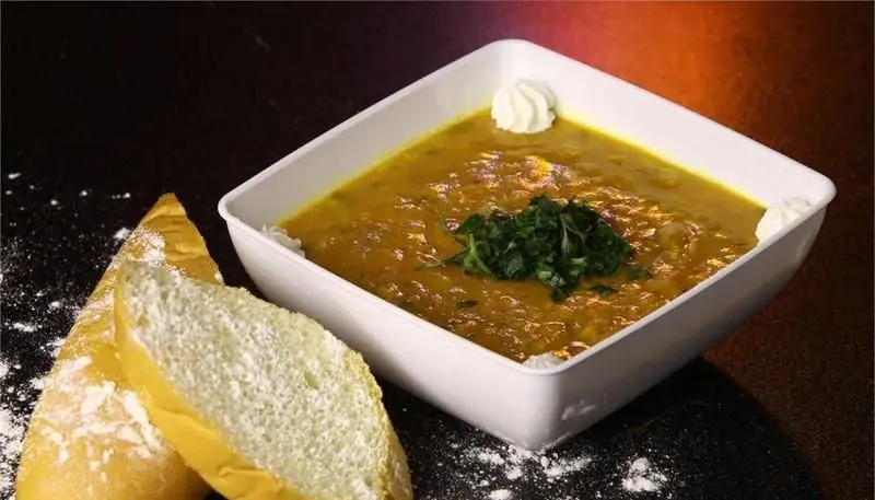 یک کاسه سوپ یا خورشت گرم و دلپذیر رستوران ایرانی شاهو، همراه با تکه‌های نان تازه، تزئین شده با سبزیجات معطر و خامه، آماده سرو.