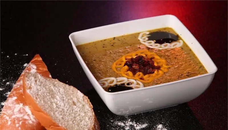 غذای سنتی و خوش طعم از رستوران ایرانی شاهو: یک کاسه حلیم یا آش غلیظ با تزئینات پیاز داغ و سس مخصوص، سرو شده با نان تازه و سفید.