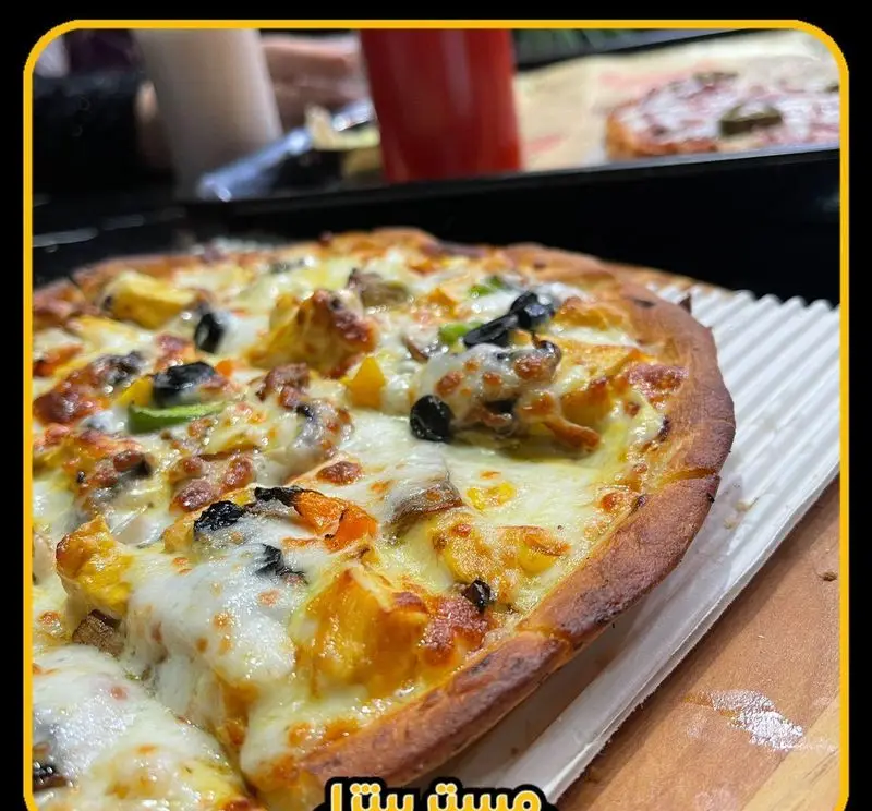 پیتزای خوشمزه مستر پیتزا با پنیر کش‌دار، تکه‌های مرغ، قارچ، زیتون سیاه و فلفل دلمه سبز. پیتزایی داغ و لذیذ برای عاشقان فست‌فود.