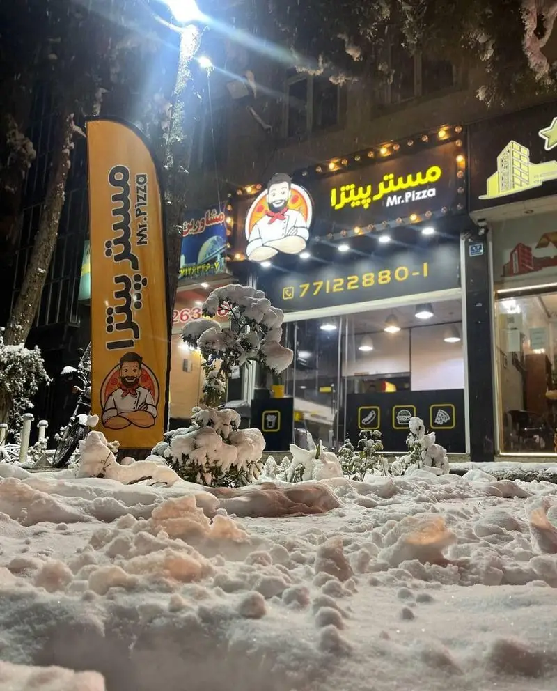 رستوران فست فود مستر پیتزا در شبی برفی، تابلوی نورانی آن به همراه لوگو و شماره تلفن برای سفارش غذا.
