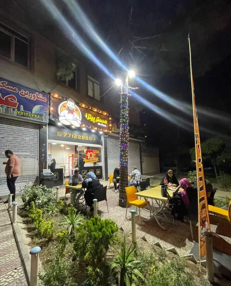 نمای شبانه رستوران مستر پیتزا، فضای باز پر از مشتری و نورپردازی جذاب. تماس برای سفارش پیتزا: ۷۷۱۲۲۸۸۰-۱.