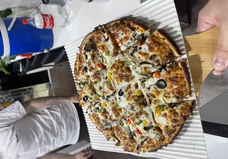 پیتزای ویژه مستر پیتزا با قارچ، سبزیجات تازه، پنیر ذوب شده، فلفل دلمه رنگی و زیتون سیاه، در حال برش برای سرو.