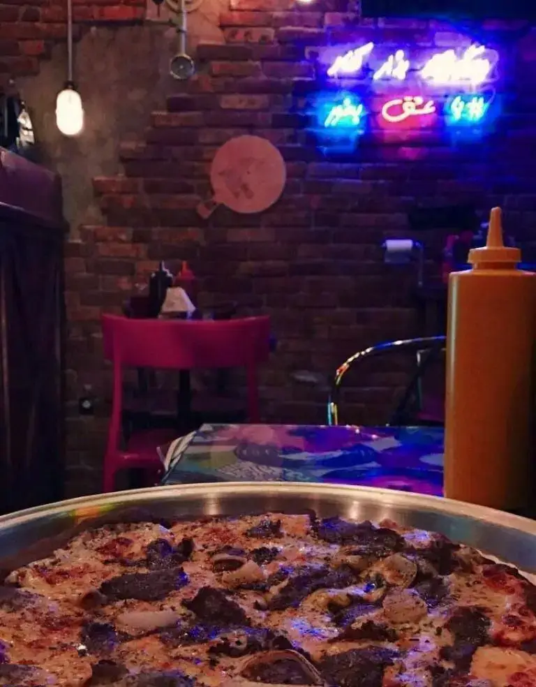 فضای داخلی رستوران چارچیز با پیتزای عالی و خوش‌منظر، دیوارهای آجری، نورپردازی خاص و تابلو نئون در محیطی گرم و صمیمی.