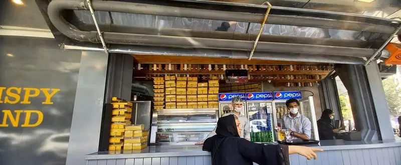 نمایی از کانتر سرزمین سوخاری هروی، نمایش محصولات غذایی در بسته بندی طلایی، با حضور پرسنل در حال خدمت رسانی در فست فود