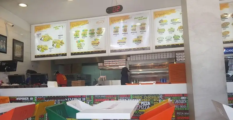 محیط داخلی شیک فست فود نامبرتن با نمایشگر منوی متنوع مرغ سوخاری، برگر و انواع ساندویچ، همراه با پرسنل در آشپزخانه.