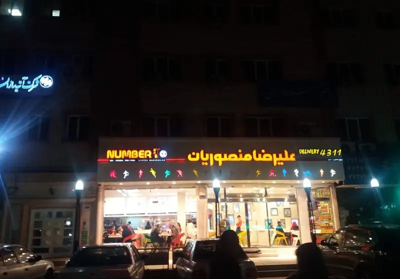 تصویر شب از فست فود نامبرتن (Number 10) علیرضا منصوریان با نورپردازی جذاب، مشتریان، تابلوی درخشان و شماره تماس دلیوری ۴۳۱۱.