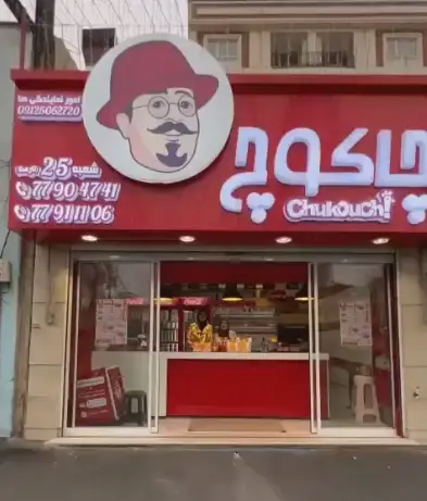 تصویری از نمای بیرونی فست فود چاکوچ، شعبه‌ای با لوگوی خاص مرد کلاهدار و شماره تماس‌ها. بهترین انتخاب برای غذای آماده و سوخاری.