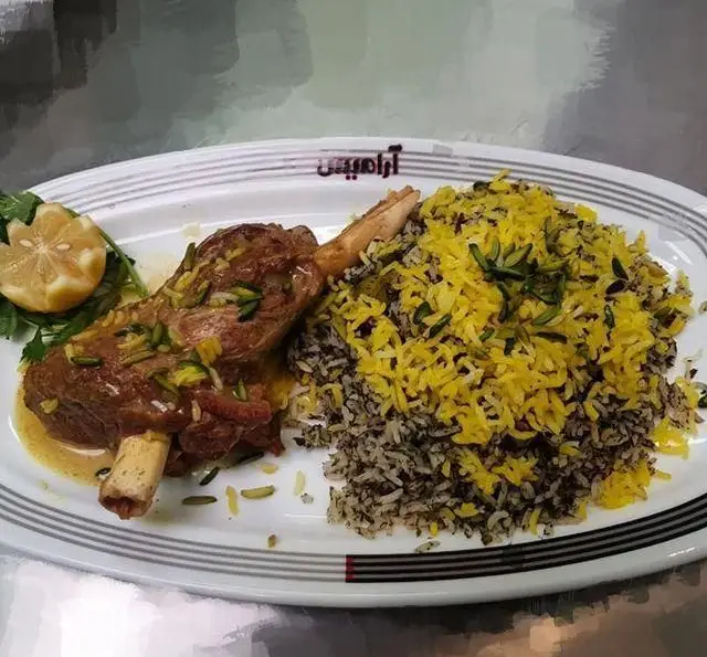 غذای خوشمزه رستوران آراميس شامل ماهیچه گوسفندی آبدار با پلو زعفرانی و سبزی پلو، تزئین شده با پسته و لیمو. لذت طعم اصیل ایرانی.