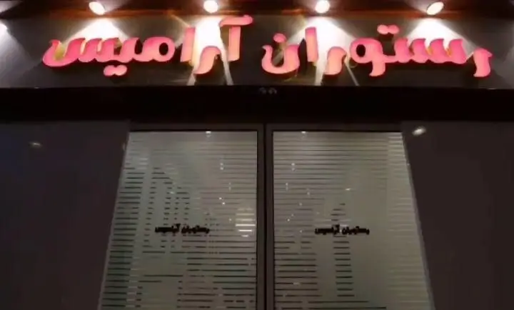 نمای بیرونی رستوران آرامیس با تابلو نئون درخشان صورتی رنگ و درب‌های ورودی شیشه‌ای مات که نام رستوران روی آنها حک شده است.