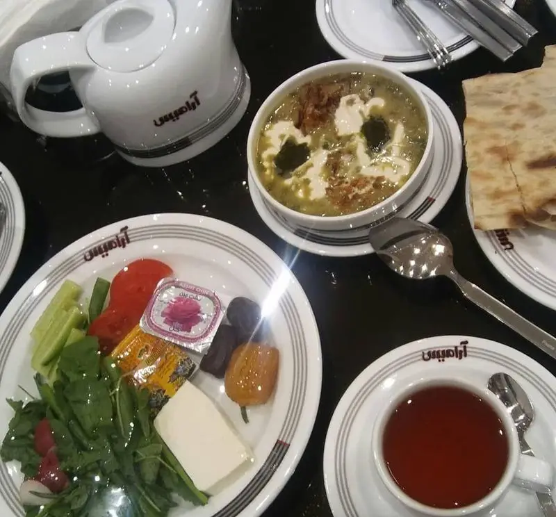 منوی صبحانه و ناهار رستوران آرامیس شامل آش رشته، چای، سبزی تازه، پنیر و نان. تجربه‌ای دلپذیر از غذای اصیل ایرانی.