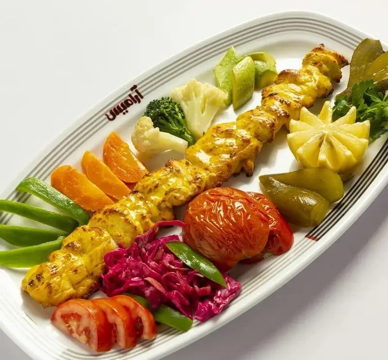 تصویری از جوجه کباب طلایی و خوش طعم رستوران آراميس همراه با مخلفات رنگارنگ، گوجه، لیمو، سبزیجات و ترشی. غذای ایرانی.