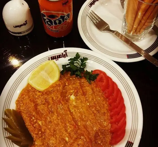 تجربه‌ای دلنشین در رستوران آرامیس: املت یا میرزا قاسمی تازه و خوش‌طعم با گوجه، لیمو و ترشی، همراه با نوشابه فنتا پرتقال.