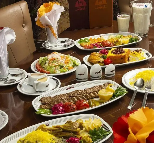 میز پر از غذاهای لذیذ ایرانی در رستوران آرامیس: کباب کوبیده، باقالی پلو با گوشت، ته چین، سالاد شیرازی، دوغ و برنج زعفرانی