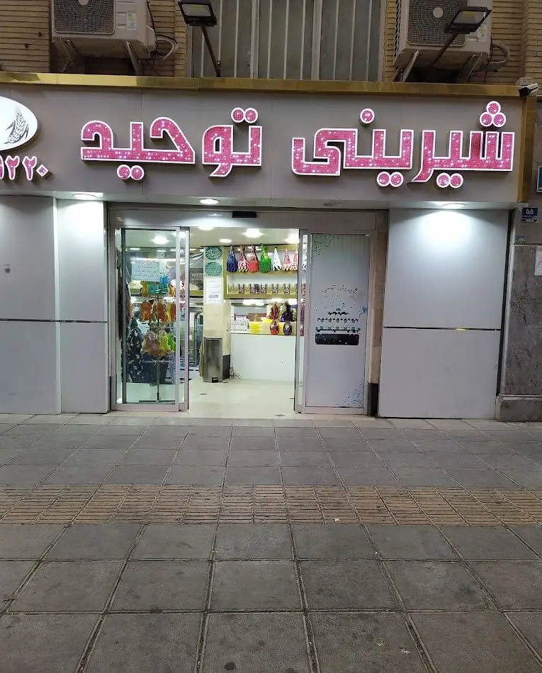نمای بیرونی جذاب فروشگاه قنادی شیرینی توحید با تابلوی روشن صورتی رنگ چشمگیر و درهای شیشه‌ای ورودی مغازه.