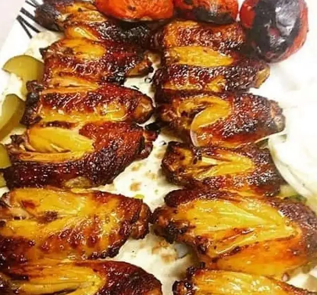 تصویری جذاب از کتف و بال کبابی طلایی و خوشرنگ، به همراه گوجه های کبابی، خیارشور و پیاز، آماده سرو در باغ رستوران سنتی گل یخ.