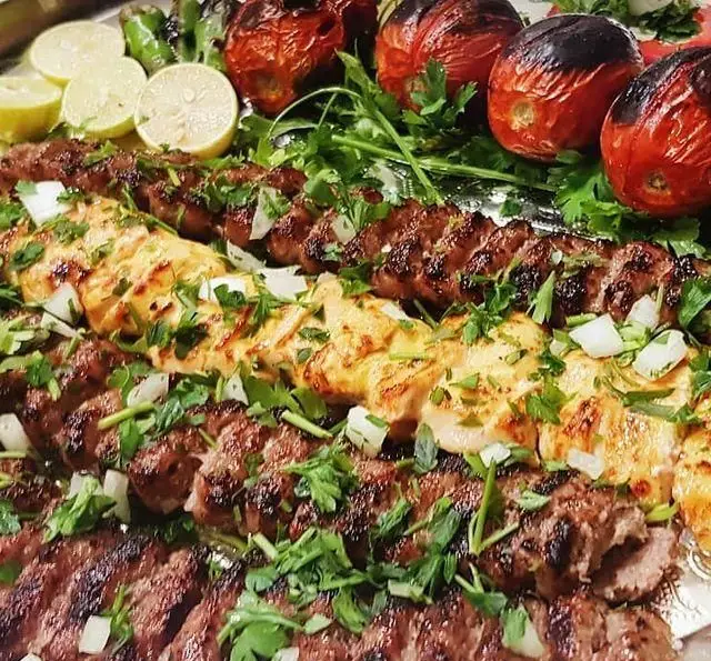 انواع کباب ایرانی لذیذ (کوبیده و جوجه کباب) با گوجه و فلفل کبابی، لیمو و سبزیجات تازه در باغ رستوران سنتی گل یخ.