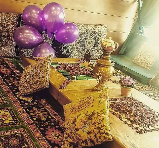 فضای سنتی و جشن با بادکنک‌های بنفش در باغ رستوران سنتی گل یخ، با سماور، فرش ایرانی و تزئینات دلنشین.